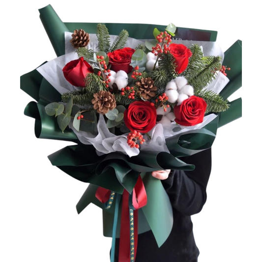 A bouquet of fresh flowers including red and white roses, lilies, and greenery, accented with festive elements. Christmas flower bouquet Dubai with roses and lilies